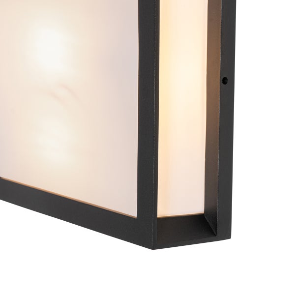 Nahaufnahme einer modernen Wandleuchte mit schwarzem Metallrahmen und weißem Diffusor, Licht eingeschaltet.