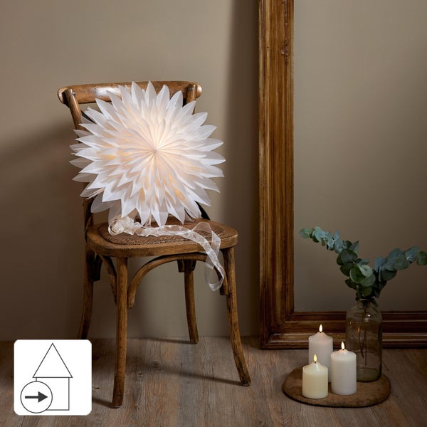 Dekorative Stehlampe mit LED-Lichtern neben einem grünen Topfbaum, Hausschuhen und einem Stuhl