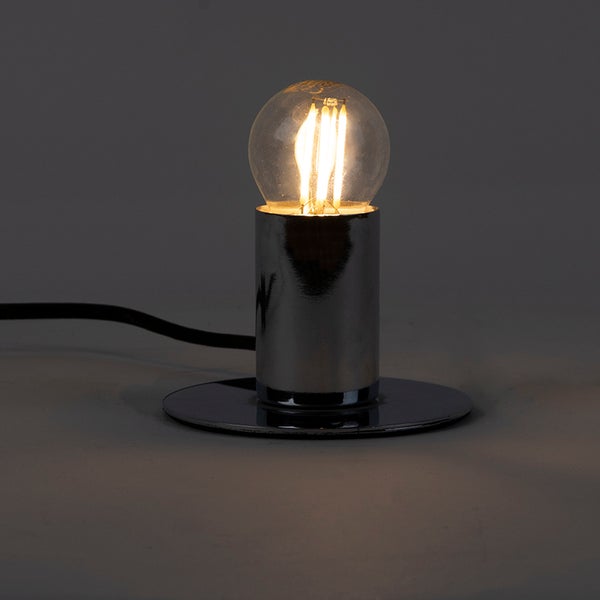 Tischleuchte aus Chrom mit rundem Standfuß und eingeschalteter LED-Filamentlampe.