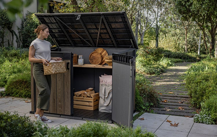 Gartenszene mit einer Frau, die einen Korb trägt und vor einem geöffneten Geräteschuppen steht, der Regale und Holzlagerung zeigt.