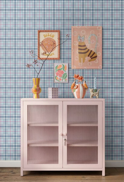 Vliestapete mit Karomuster in Blau, Weiß und Rosa an einer Wand hinter einer rosa Metallvitrine mit verschiedenen Dekorationsartikeln.