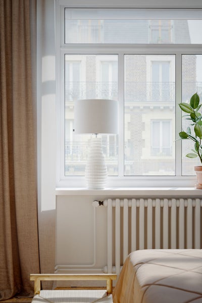 Helles Zimmer mit Heizkörper, Lampe und Fenster mit Blick auf ein Gebäude