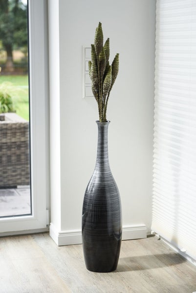 Moderne Bodenvase mit strukturierter Oberfläche und Trockenpflanzen in einer hellen Zimmerecke neben einem Fenster mit Plissee.