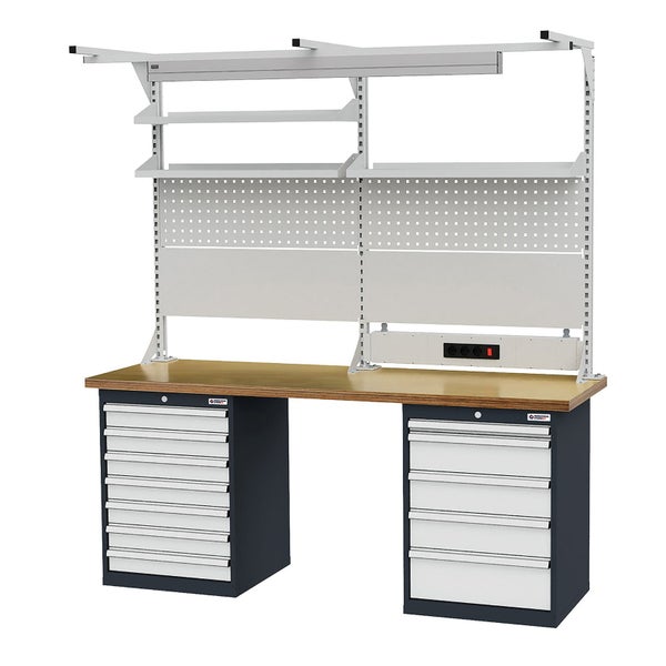 Olivenbaum mit dickem Stamm in großem Topf auf Holzpalette in heller Gärtnerei, umgeben von Palmen und Nadelbäumen.