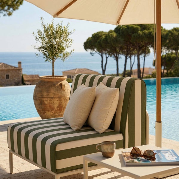 Gestreifter Garten-Loungesessel mit beigen Kissen auf einer Terrasse am Pool, daneben ein Beistelltisch unter einem Sonnenschirm.