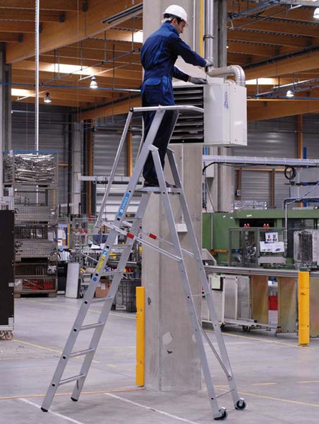 Eine Person steht auf einer TANGEN Leiter in einer Industriehalle und arbeitet an einer Klimaanlage.