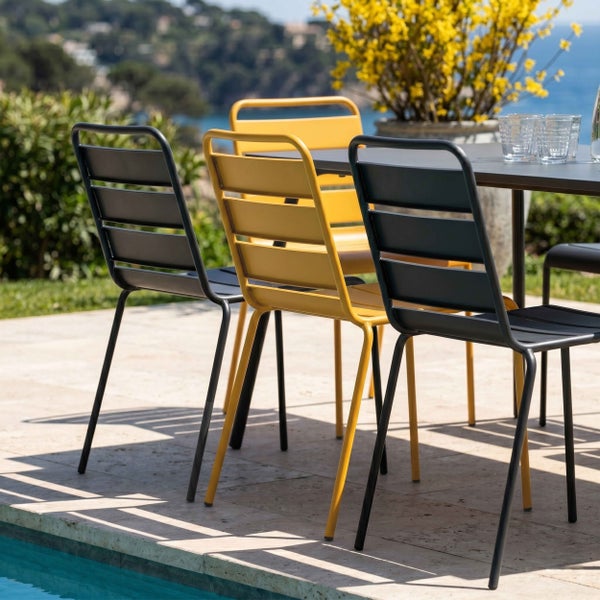 Moderne Gartenmöbel aus Metall mit Lattenstühlen und Tisch auf einer Steinterrasse am Pool, Hintergrund mit Meerblick und gelben Blumen.