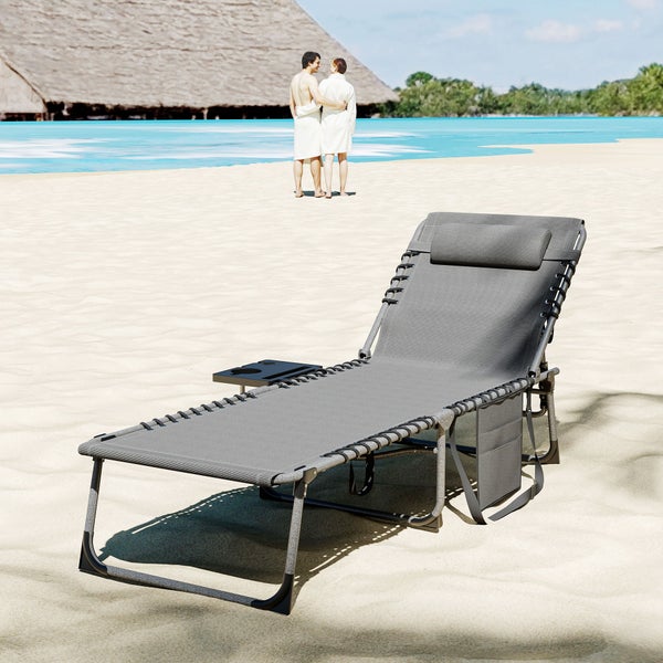 Sonnenliege mit Kopfkissen, seitlicher Ablage und Tasche in einer hellen Strandszene mit Sand und Wasser.
