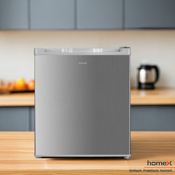 Silberfarbener Minikühlschrank auf einem Holztisch vor einer Küchenzeile