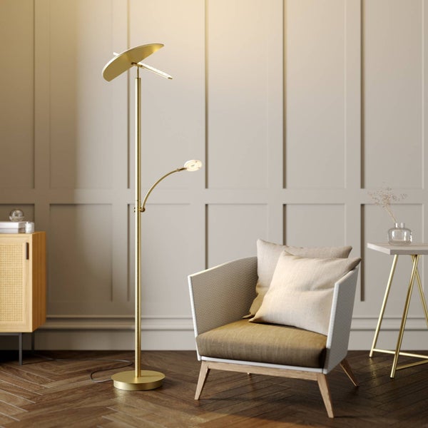 Messingfarbene Stehleuchte mit Deckenfluter und Lesearm in einem hellen Wohnzimmer neben einem Sessel vor einer Wand mit Paneelen.