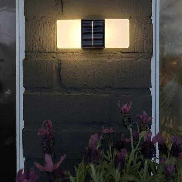 Solarleuchte an einer Mauer mit Lavendel im Vordergrund.