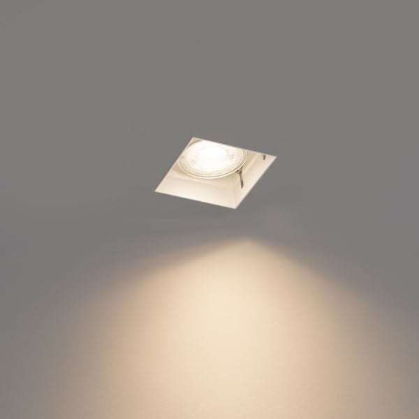 Quadratischer Einbaustrahler mit eingeschaltetem Leuchtmittel und warmweißem Lichtkegel an der Wand.