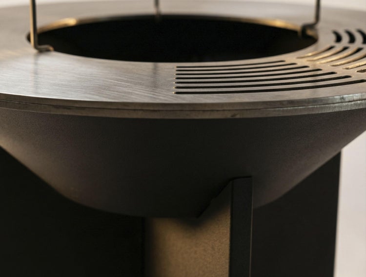 Detail einer runden Feuerschale aus Metall mit breitem Grillring und Belüftungsschlitzen.