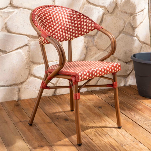 Bistrostuhl mit Armlehnen und rot-beigem Geflecht auf einer Holzterrasse vor einer hellen Steinwand im Außenbereich.