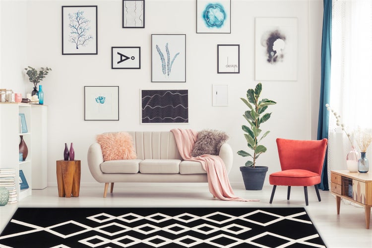Wohnzimmer mit hellem Sofa, rotem Sessel und einem auffälligen Teppich mit geometrischem Rautenmuster in einem modernen eingerichteten Raum.
