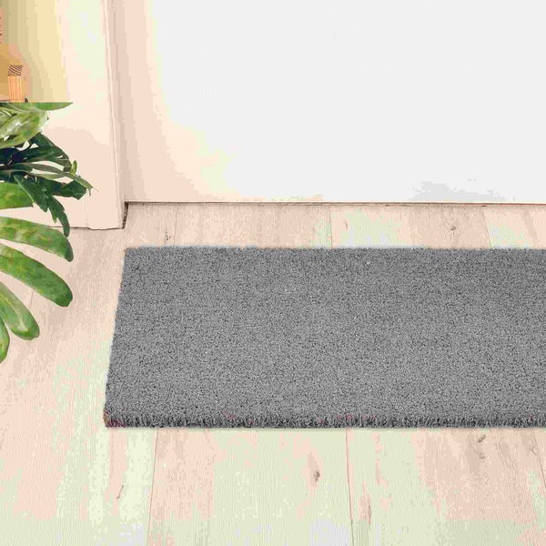 Graue Fußmatte vor einer weißen Tür auf hellem Holzboden