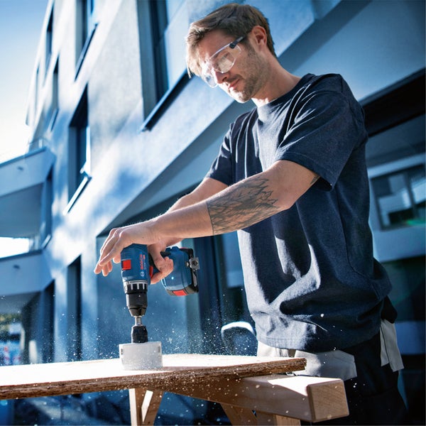 Ein Mann benutzt einen Akku-Bohrschrauber von Bosch, um an einem Regal zu arbeiten. Er trägt eine Schutzbrille.