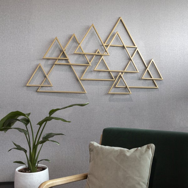 Geometrische Wanddekoration aus Metall mit Dreiecken in Bergoptik über einem Sessel und einer Zimmerpflanze.