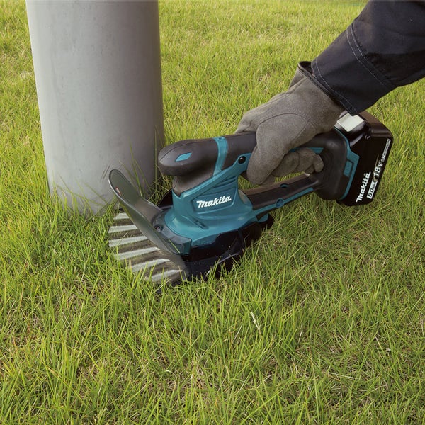 Makita Akku-Grasschere 18 Volt beim Schneiden von Rasenkanten an einem Pfosten.