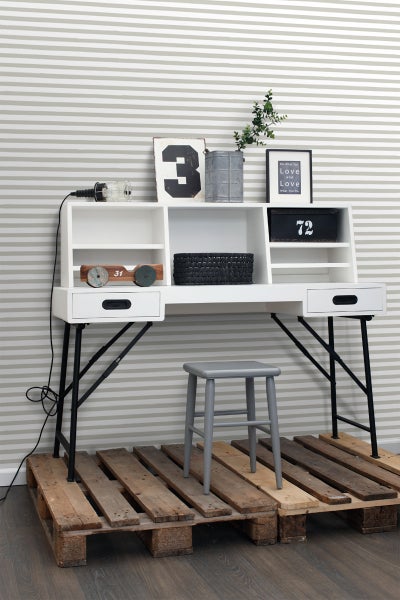 Heller Schreibtisch mit Ablagefächern, Schubladen und schwarzem Metallgestell vor gestreifter Tapete