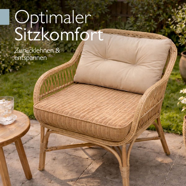Gartensessel aus Rattan mit weichem Sitzpolster und Rückenkissen auf einer Terrasse stehend.
