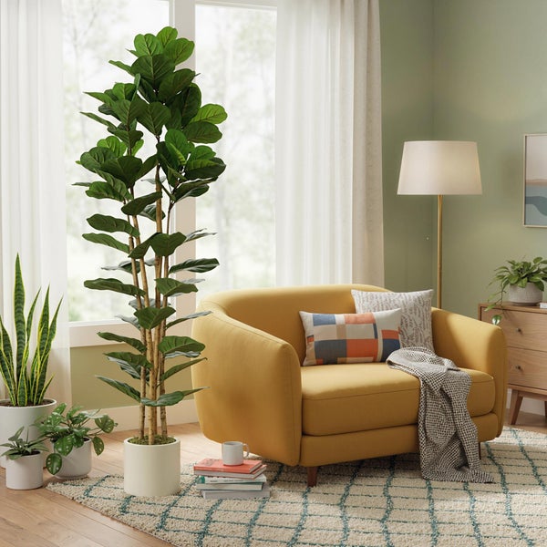 Helles, modernes Wohnzimmer mit einer großen künstlichen Geigenfeige, einem gelben Sessel mit Kissen und mehreren Zimmerpflanzen auf einem Teppich.