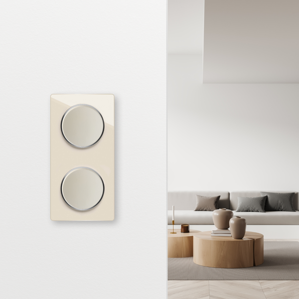 Doppelwippschalter mit zwei runden Tasten an einer hellen Wand mit moderner Wohnzimmereinrichtung im Hintergrund