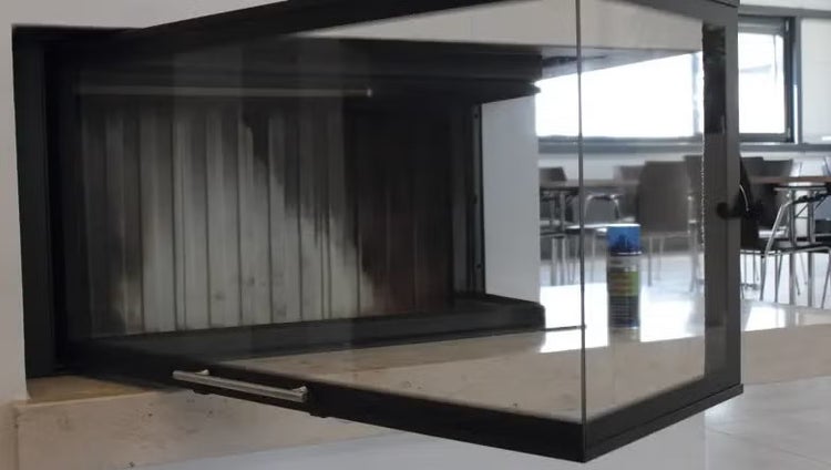 Kamineinsatz mit geöffneter Glastür und Spiegelung einer Sprühdose Kaminglasreiniger.