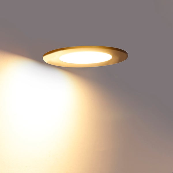 Runder LED Einbaustrahler in Gold mit warmweißem Lichtkegel an einer Wand.