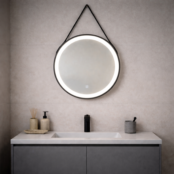 Runder LED-Badezimmerspiegel mit schwarzem Aufhängungsband über einem Waschtisch mit weißem Waschbecken, schwarzer Armatur und Badzubehör.