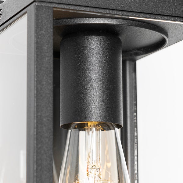 Nahaufnahme der Metallfassung und des Leuchtmittels einer schwarzen Außenwandleuchte im Laternendesign.