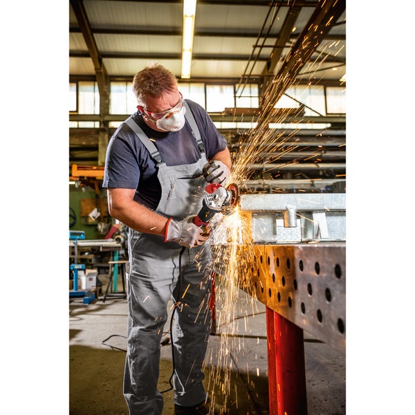 Handwerker mit Schutzausrüstung trennt ein Metallstück mit einem Winkelschleifer in einer Werkstatt, wobei Funkenflug entsteht.