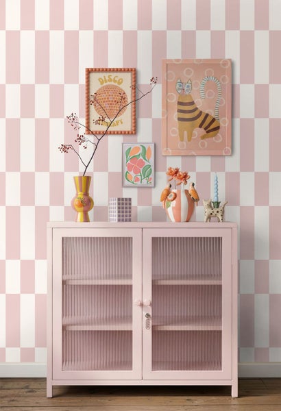 Moderner Wohnbereich mit rosafarbenem Metallschrank und Riffelglas vor einer karierten Tapete in Rosa und Weiß mit dekorativen Vasen.