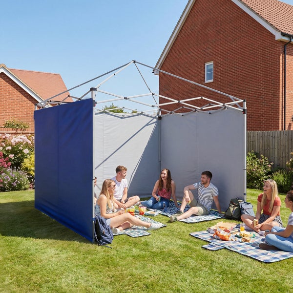 Eine Gruppe von Personen bei einem Picknick im sonnigen Garten unter einem Faltpavillon mit zwei montierten Seitenwänden auf einer Rasenfläche.