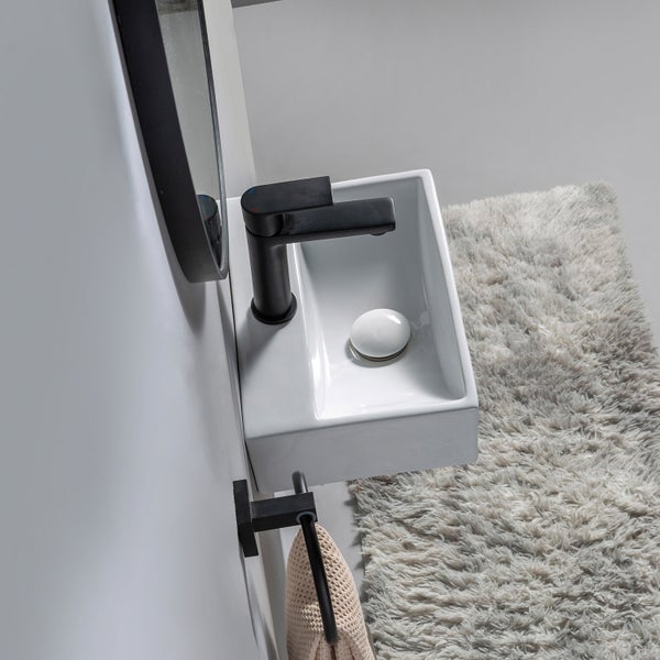 Ein kleines weißes Keramik Waschbecken mit einer modernen schwarzen Armatur, einem Handtuchhalter und einem Spiegel im Badezimmer.