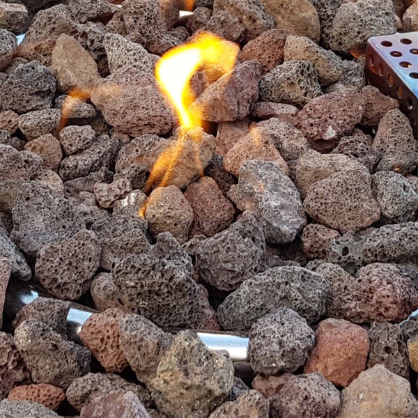 Poröse Lavasteine in einer Feuerstelle mit einer brennenden Flamme über einem Gasbrenner.