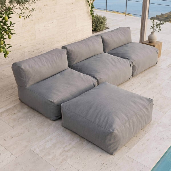 Modulares Garten-Lounge-Set aus grauem Stoff mit drei Sitzelementen und einem Hocker auf einer Steinterrasse mit Blick auf das Meer.