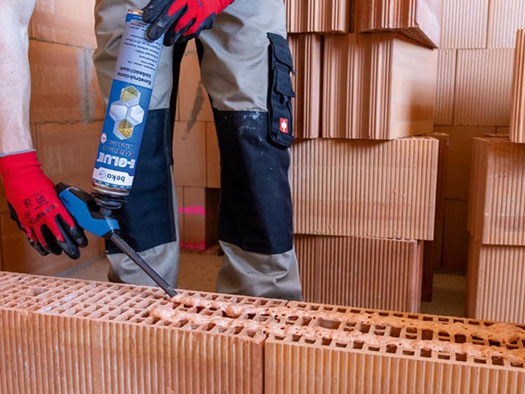 Handwerker beim Auftragen von Beko F-Glue Konstruktionsklebeschaum auf einen Ziegelstein mit einer Schaumpistole auf einer Baustelle