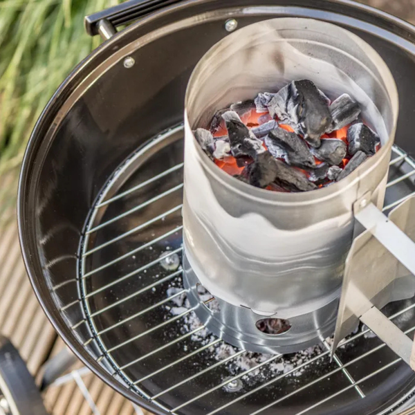 Anzündkamin aus Metall mit glühender Holzkohle auf einem Grillrost in einem Kugelgrill.