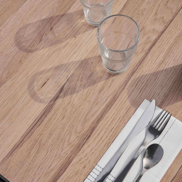 Nahaufnahme einer Tischplatte in Holzoptik mit zwei Gläsern und Besteck auf einer Serviette.