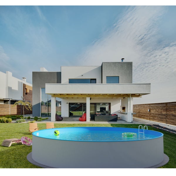 Moderner Garten mit rundem Aufstellpool, Rasen, Holzliegen und einem zweistöckigen Haus mit Terrasse und Außenmöbeln.