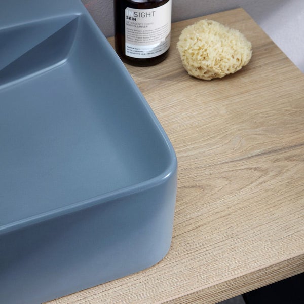 Blaues mattes Waschbecken auf einer hölzernen Waschtischplatte mit einem Naturschwamm und einer Flasche.