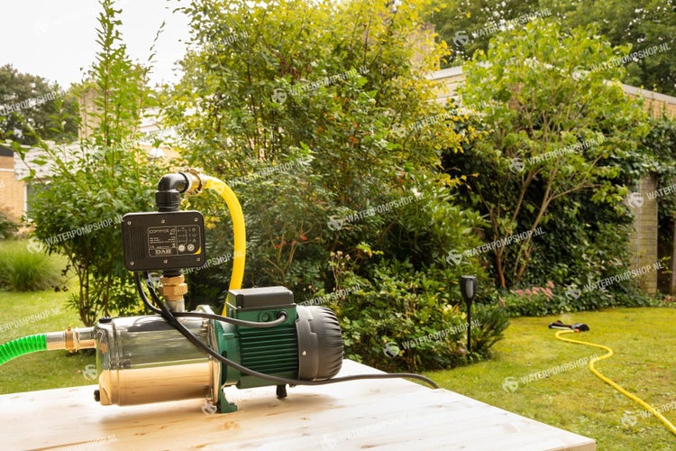Hauswasserwerk mit Steuerung auf einem Gartentisch vor Grünanlage