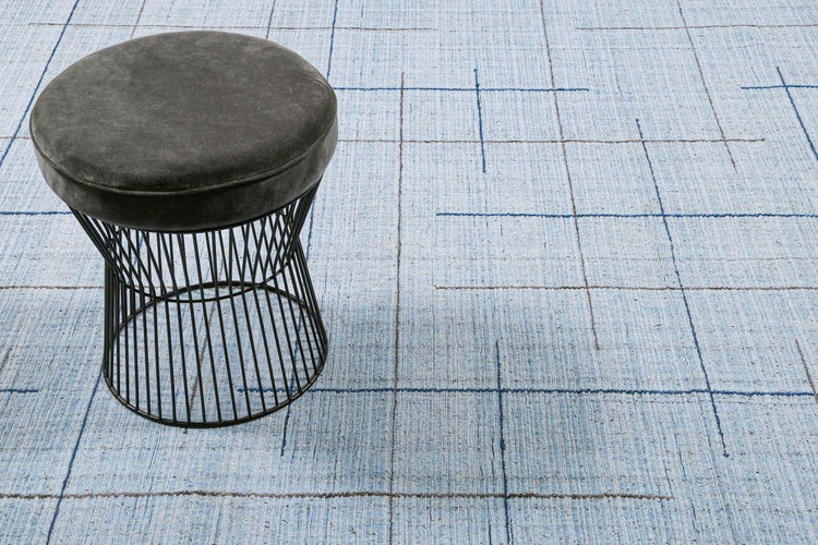 Hellblauer Teppich mit Gittermuster in einem modern eingerichteten Wohnzimmer mit beigem Sofa, Sessel und Dekokissen.