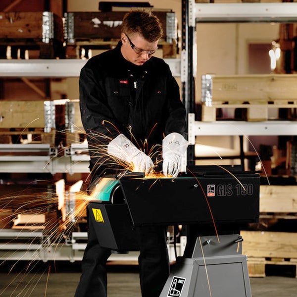 Handwerker mit Schutzbrille und Handschuhen bedient eine Bandschleifmaschine GRIT GIS 150 in einer Werkstatt bei Funkenflug.