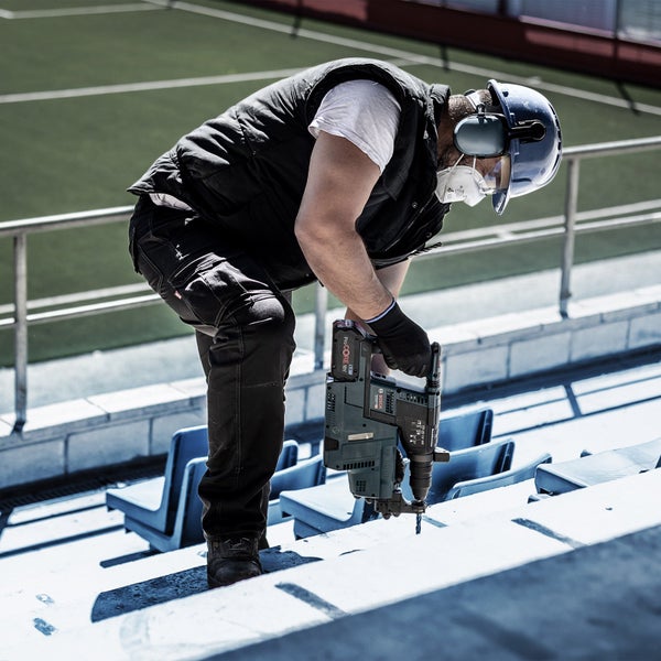 Ein Mann bohrt mit einem Bohrhammer ein Loch in eine Betonplatte in einem Stadion.