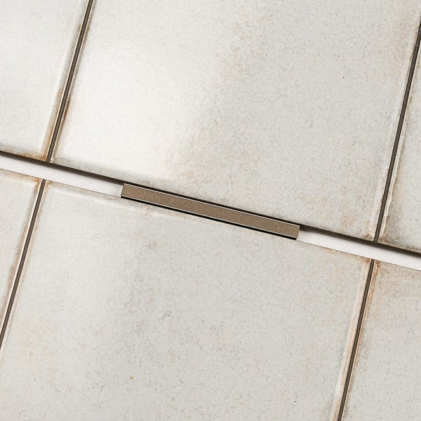 Fliesenkreuz mit Metalloberfläche zwischen quadratischen Fliesen verlegt