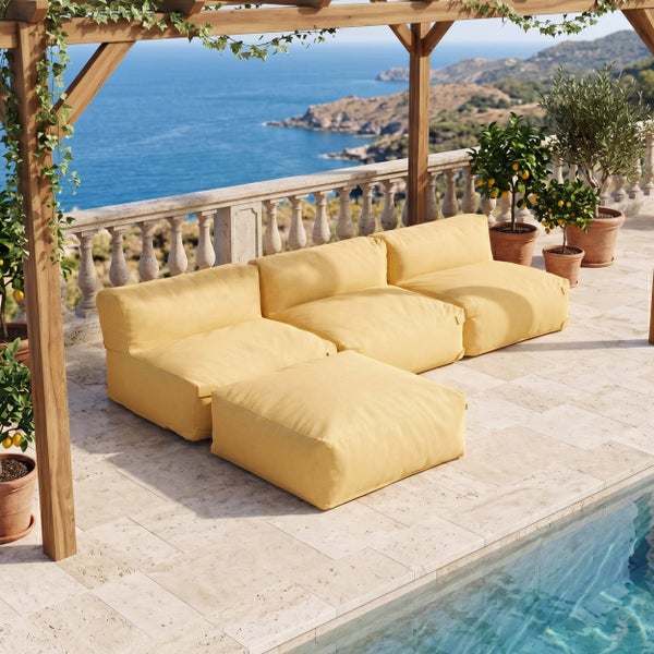 Modulare Outdoor-Lounge mit gelben Polsterelementen auf einer hellen Steinterrasse mit Meerblick unter einer hölzernen Pergola am Pool.