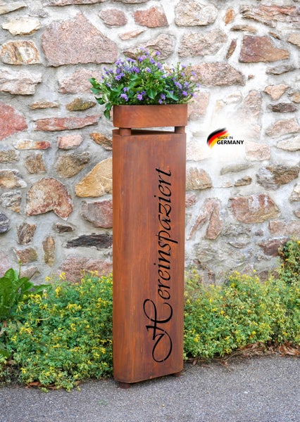 Rostige Dekosäule aus Metall mit Pflanzschale und Schriftzug Hereinspaziert vor einer Steinmauer mit Made in Germany Siegel