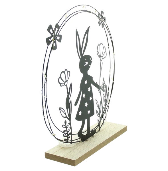 Dekorative Osterdekoration mit Hasenmotiv und Blumen in einem runden Rahmen auf einem Holzsockel